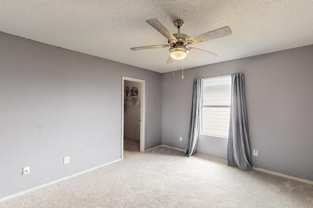 spare room with baseboards, ceiling fan, light carpet, and a textured ceiling