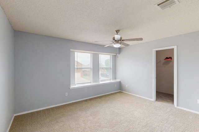 unfurnished bedroom with a walk in closet, a textured ceiling, visible vents, carpet floors, and a closet