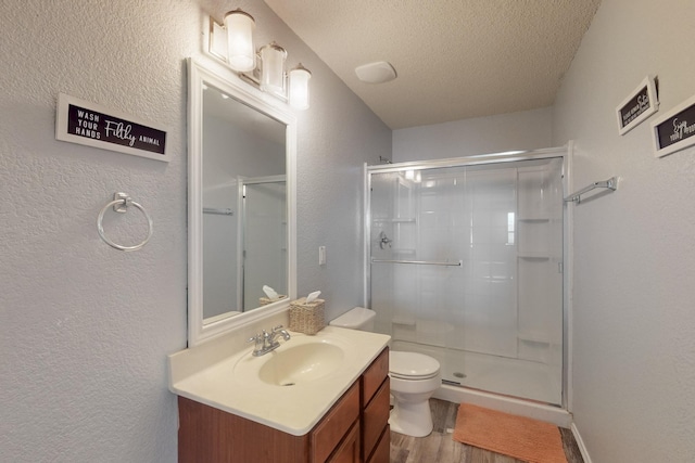 full bath with a textured ceiling, a shower stall, wood finished floors, vanity, and toilet