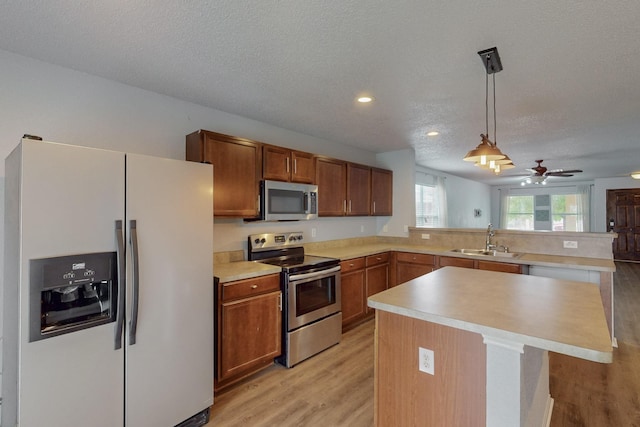 kitchen featuring a sink, light countertops, light wood-style flooring, stainless steel appliances, and a peninsula
