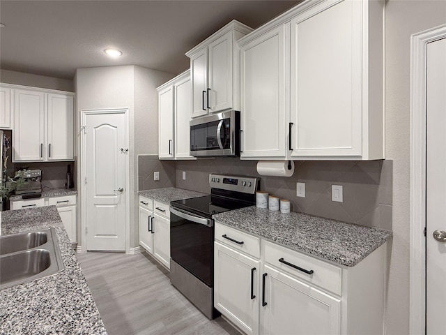 kitchen featuring light wood-style floors, stainless steel appliances, recessed lighting, white cabinetry, and backsplash