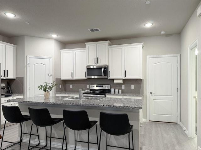 kitchen with visible vents, a breakfast bar, white cabinetry, tasteful backsplash, and stainless steel appliances