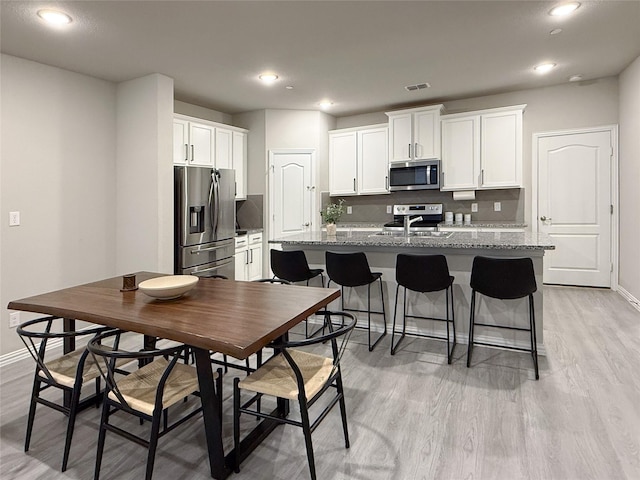 kitchen featuring a center island with sink, baseboards, stainless steel appliances, and white cabinets