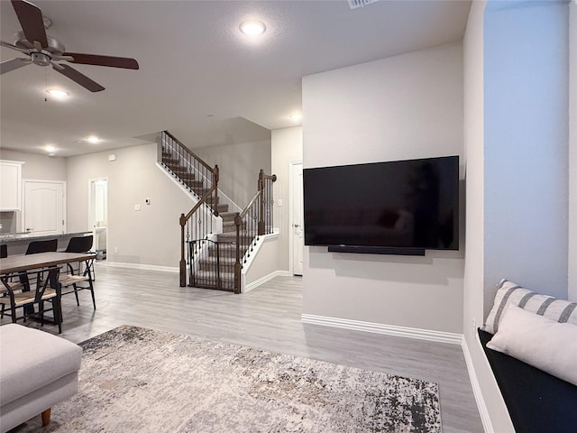 living area featuring ceiling fan, stairway, baseboards, light wood finished floors, and recessed lighting
