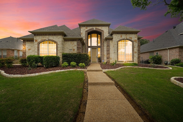 view of front of house with stone siding, a yard, and roof with shingles