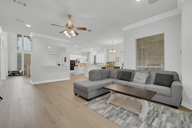 living area featuring light wood-type flooring, ceiling fan, a chandelier, ornamental molding, and baseboards