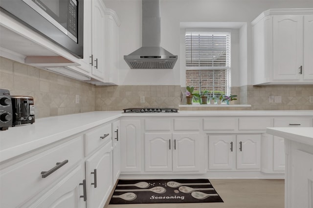 kitchen featuring wall chimney exhaust hood, stainless steel appliances, white cabinets, and backsplash