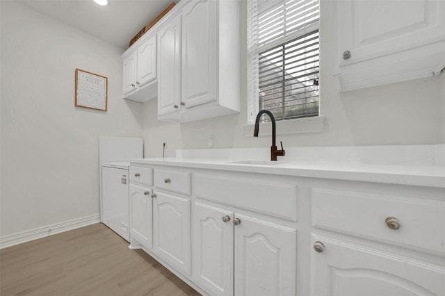 kitchen with white cabinetry, a sink, light wood-style floors, light countertops, and baseboards