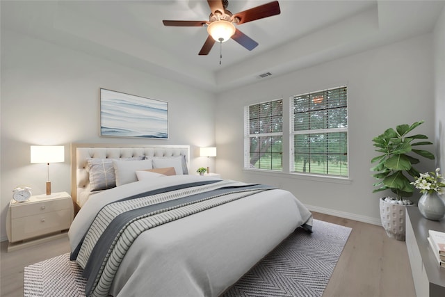 bedroom with a raised ceiling, baseboards, light wood-style floors, and a ceiling fan