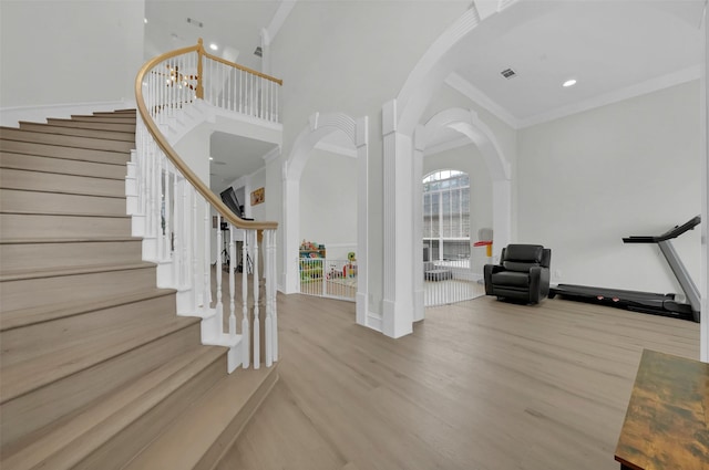 foyer entrance featuring crown molding, arched walkways, wood finished floors, stairway, and a towering ceiling
