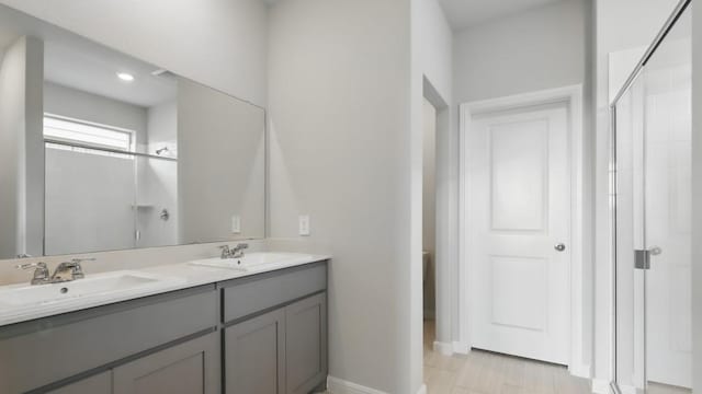 full bathroom with double vanity, a sink, baseboards, and a shower stall