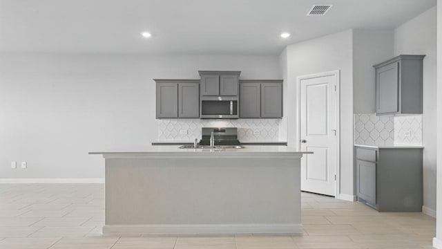 kitchen featuring decorative backsplash, gray cabinets, visible vents, a sink, and stainless steel microwave