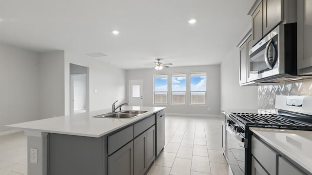 kitchen with light countertops, gray cabinets, a sink, appliances with stainless steel finishes, and backsplash