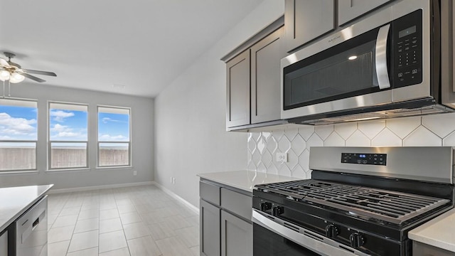 kitchen with decorative backsplash, ceiling fan, gray cabinetry, baseboards, and stainless steel appliances