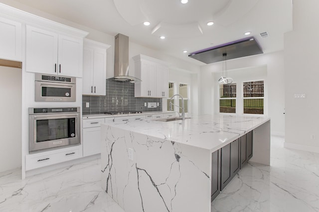 kitchen with decorative backsplash, a large island, wall chimney exhaust hood, white cabinets, and a sink