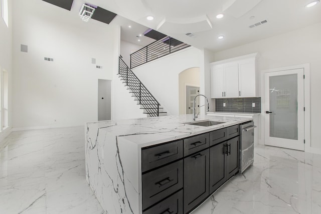 kitchen featuring white cabinets, a sink, marble finish floor, visible vents, and a center island with sink