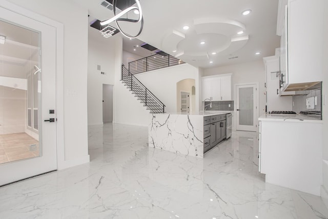 kitchen with visible vents, a kitchen island with sink, arched walkways, white cabinets, and a sink