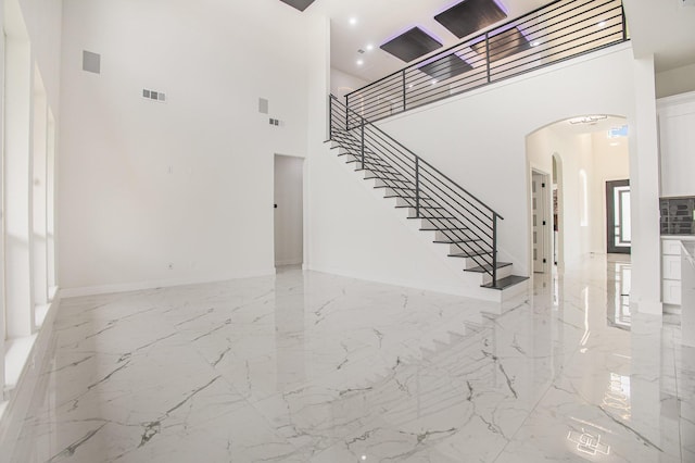 unfurnished living room featuring arched walkways, marble finish floor, a towering ceiling, visible vents, and stairway