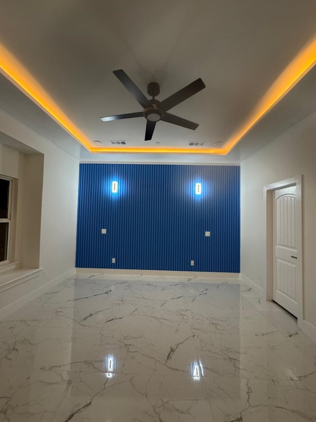 empty room featuring baseboards, a ceiling fan, a raised ceiling, and marble finish floor