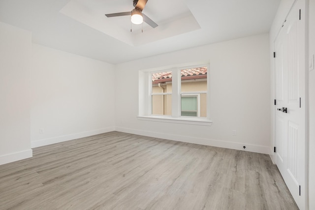unfurnished room featuring a ceiling fan, baseboards, light wood finished floors, and a raised ceiling