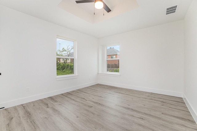 spare room with a healthy amount of sunlight, a ceiling fan, wood finished floors, and visible vents