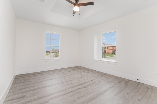 empty room featuring baseboards, a healthy amount of sunlight, a raised ceiling, and wood finished floors