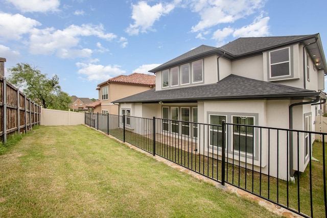 back of house featuring a lawn, a shingled roof, a fenced backyard, and stucco siding