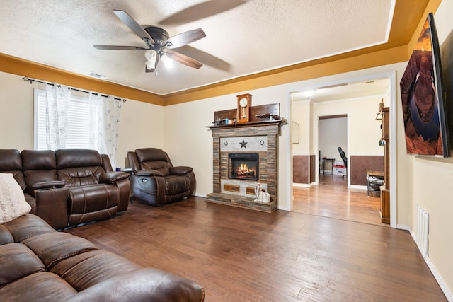 living area featuring a fireplace, a textured ceiling, a ceiling fan, wood finished floors, and visible vents