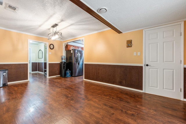 spare room featuring an inviting chandelier, a textured ceiling, a wainscoted wall, wood finished floors, and visible vents