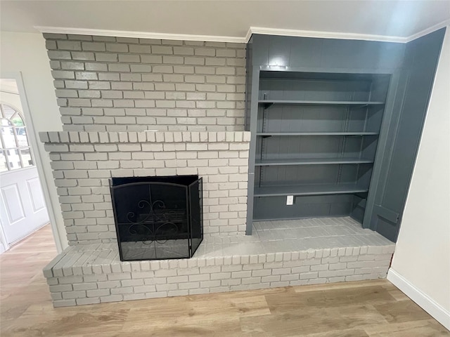 detailed view of crown molding, wood finished floors, a brick fireplace, and baseboards