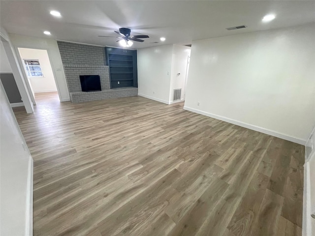 unfurnished living room with baseboards, recessed lighting, wood finished floors, built in shelves, and a brick fireplace