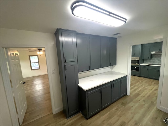 kitchen featuring light wood finished floors, decorative backsplash, light countertops, ceiling fan, and under cabinet range hood