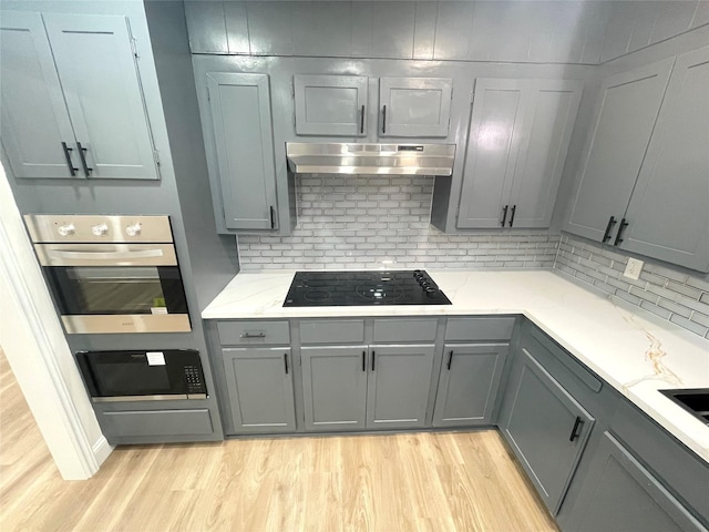 kitchen with black appliances, under cabinet range hood, gray cabinets, and backsplash