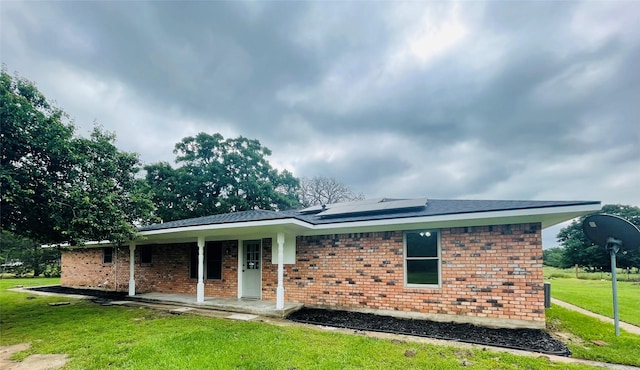 back of property featuring a yard, solar panels, a porch, and brick siding