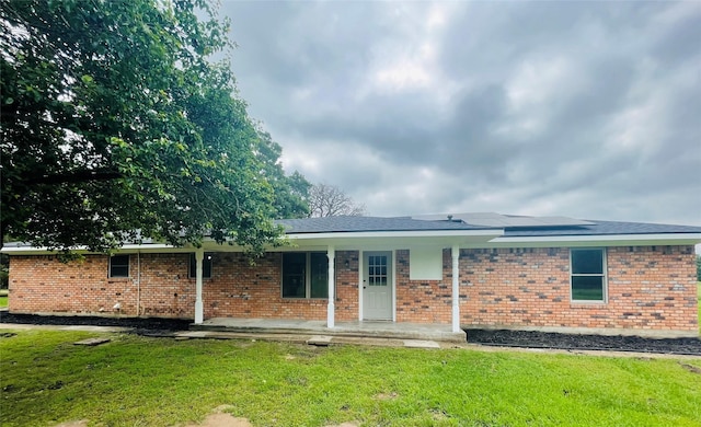 view of front facade featuring a front lawn, roof mounted solar panels, covered porch, and brick siding