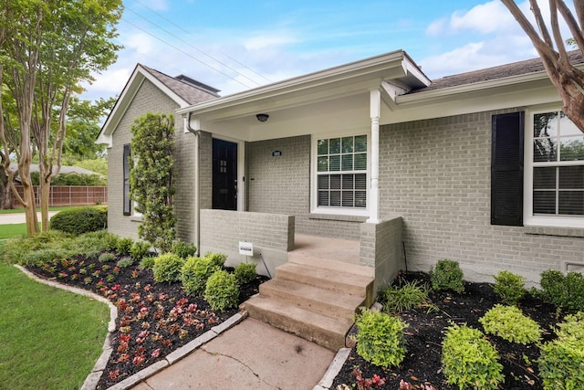 view of exterior entry with brick siding and fence