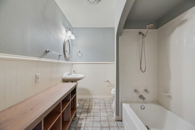 bathroom with toilet, shower / bath combination, wainscoting, and a sink
