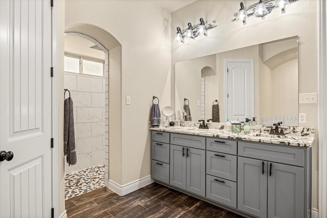full bath with a tile shower, double vanity, a sink, and wood finished floors