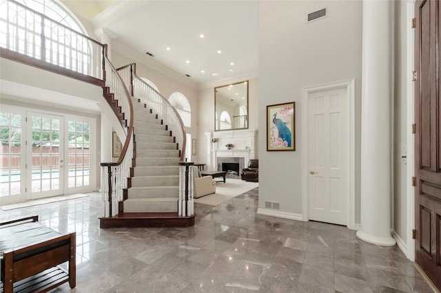 entryway with crown molding, a high ceiling, visible vents, and a fireplace