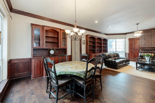 dining area featuring a wainscoted wall, ornamental molding, ceiling fan with notable chandelier, and dark wood finished floors