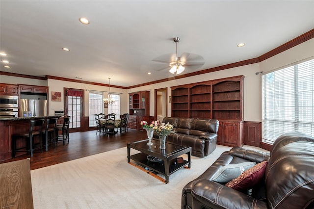 living area with crown molding, wood finished floors, recessed lighting, a wainscoted wall, and ceiling fan with notable chandelier