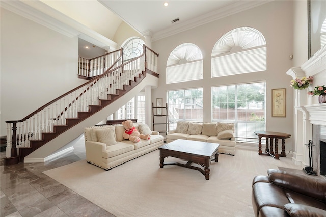 living area with visible vents, ornamental molding, a towering ceiling, a fireplace, and stairway