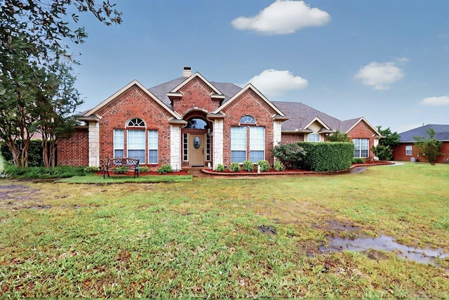ranch-style home featuring brick siding, a chimney, and a front yard