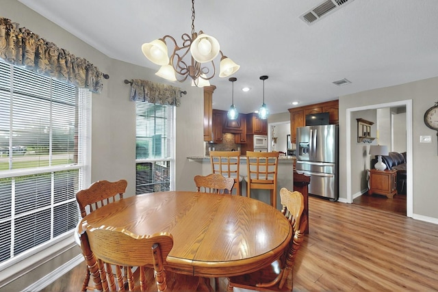 dining room featuring a chandelier, baseboards, visible vents, and light wood finished floors
