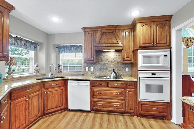 kitchen with a sink, premium range hood, light wood-type flooring, and white appliances