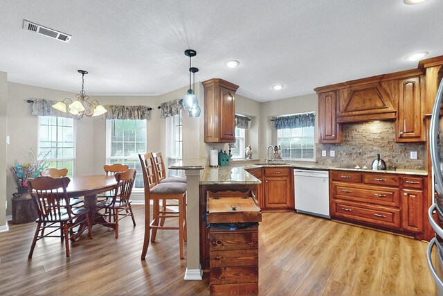 kitchen with white dishwasher, a sink, a peninsula, a notable chandelier, and light wood-style flooring