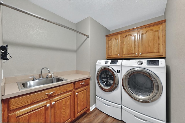laundry area featuring wood finished floors, a textured ceiling, a sink, cabinet space, and independent washer and dryer
