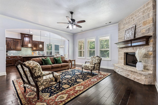 245 Prairie Oak Ct, Burleson, TX 76028 - living area featuring dark wood-style flooring, ceiling fan, a textured ceiling, a stone fireplace, and crown molding