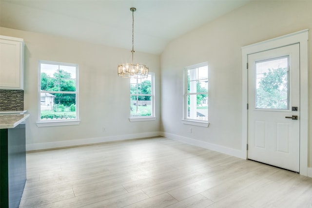 unfurnished dining area featuring baseboards, lofted ceiling, light wood-style flooring, and a chandelier