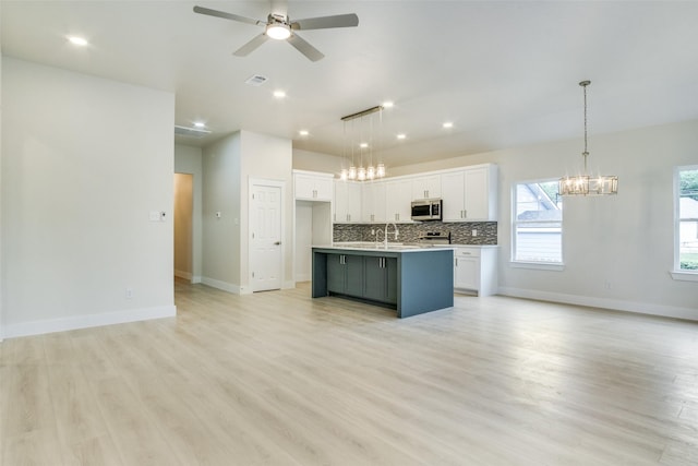 kitchen featuring open floor plan, white cabinetry, stainless steel microwave, tasteful backsplash, and ceiling fan with notable chandelier